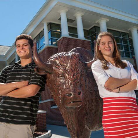 two students pose by statue of a bison