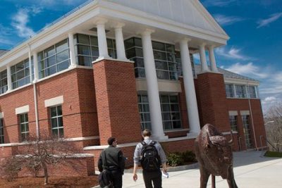 two students walking by a statue of a bison