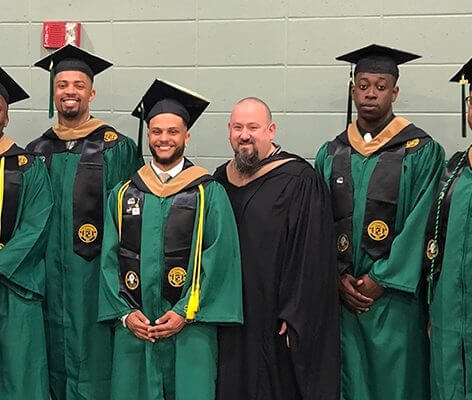 Marc Creegan standing with 7 Nichols College graduates in graduation gowns