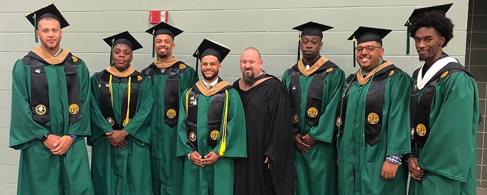 Marc Creegan standing with 7 Nichols College graduates in graduation gowns