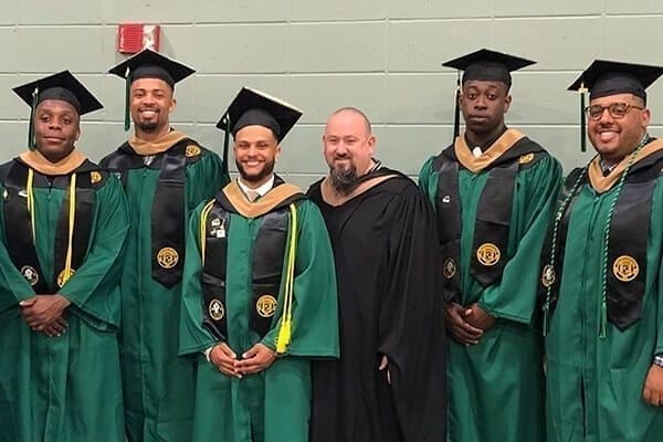 Marc Creegan standing with 7 Nichols College graduates in graduation gowns