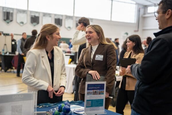 Two Nichols College students in professional attire laughing together at a career and internship fair booth