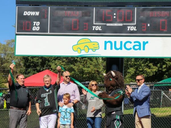 Members of the Dagesse family with President Sulmasy, cutting the ribbon for the new video scoreboard on Vendetti Field at Nichols College.