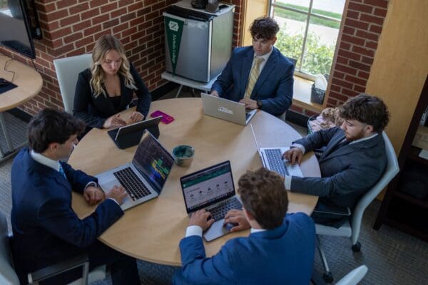 Students in professional attire collaborate around a conference table with laptops during a Bison Consulting experiential learning session.