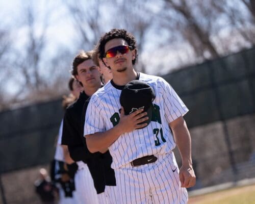 A Nichols College baseball player holds his cap to his chest during the national anthem before a game.