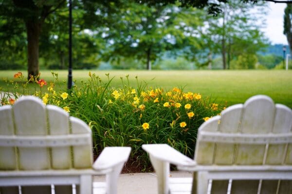 Two white Adirondack chairs face a garden of yellow and orange flowers on the Nichols College campus quad.