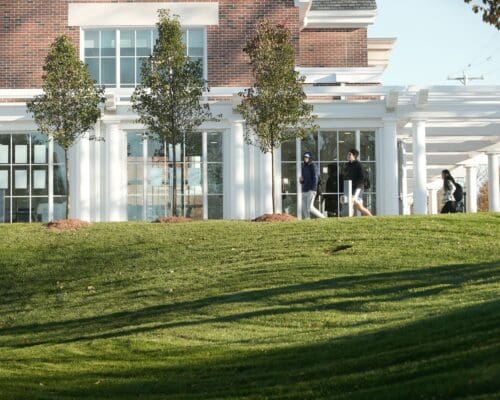 Students walk toward the entrance of Lombard Dining Hall beneath the white pergola at Nichols College.