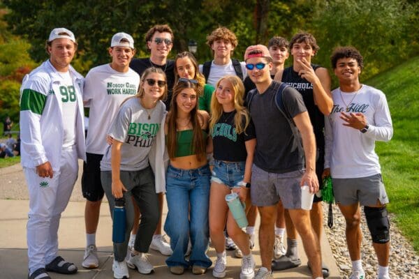 A large group of Nichols College students in Bison Pride and school spirit apparel pose together outdoors on campus.