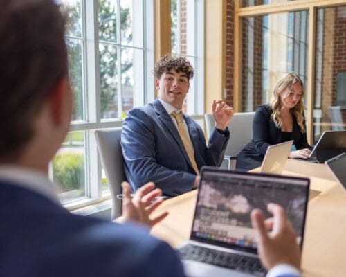 Students in professional attire collaborate around a conference table with laptops during a Bison Consulting experiential learning session.