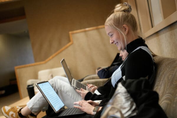 A student smiles while working on a laptop in a campus lounge at Nichols College.