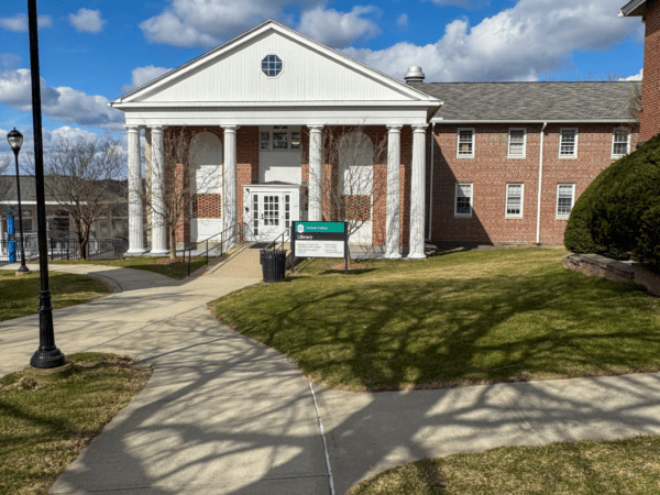 The exterior of the Nichols College library, a white-columned brick building, on a bright winter day with a clear blue sky.