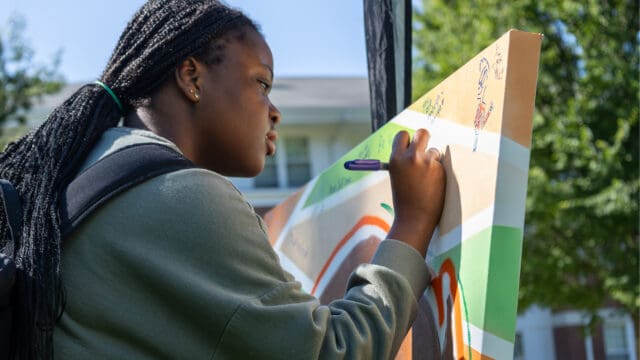 A student writes a message of inspiration on the bison mural at the Wellness Fair.