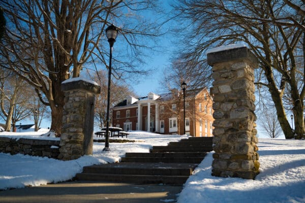 Budleigh Hall, a brick colonial-style building on the Nichols College campus, surrounded by snow on a clear winter day.
