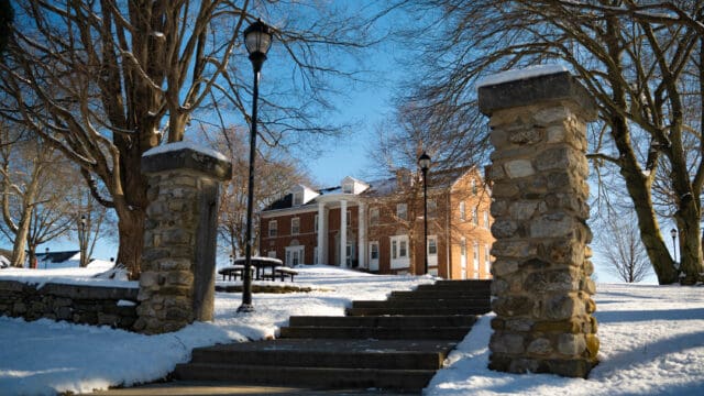 Budleigh Hall, a brick colonial-style building on the Nichols College campus, surrounded by snow on a clear winter day.
