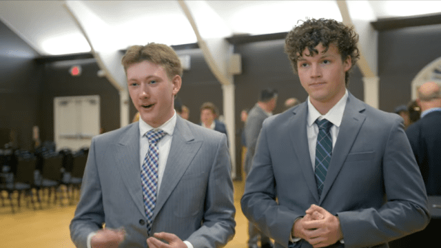 Two students dressed in business attire stand and address the camera at the 2026 Bison Pitch Competition at Nichols College