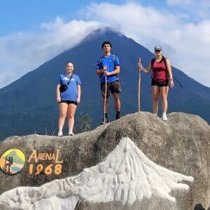 Three Nichols College students stand atop a rock with Arenal Volcano in Costa Rica behind them far in the distance.