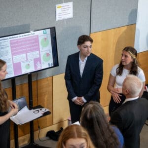 Three Nichols College students present their research project on AI and narrative truth to a faculty member at an academic research symposium