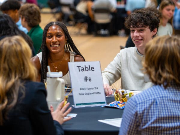 Students and an alumna sit around a circular table smiling and engaged in a group discussion during a "Second Year Success" networking session.