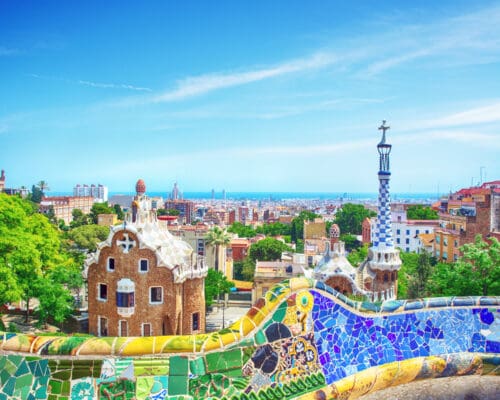 Colorful mosaic benches and Gaudí architecture at Park Güell in Barcelona, Spain, with the city skyline visible in the background